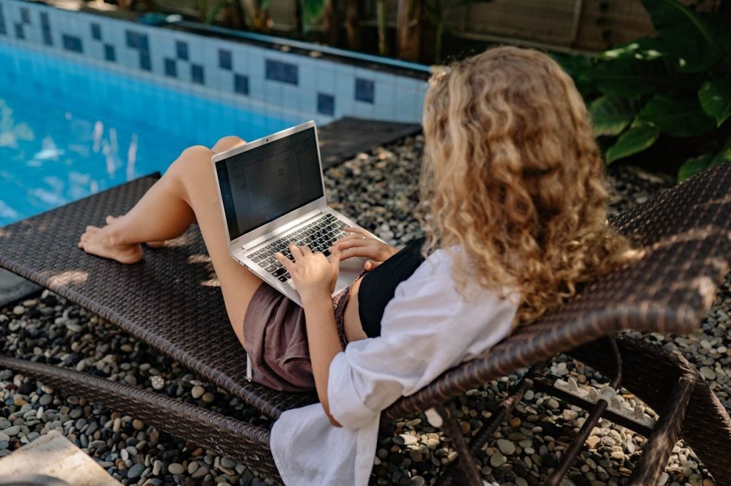 A woman is working on a laptop next to the pool.